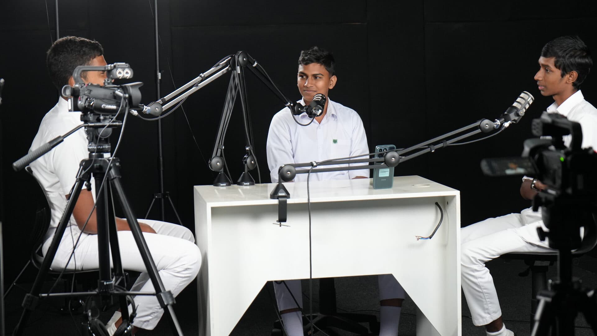 Three students in a podcast recording session with cameras and microphones